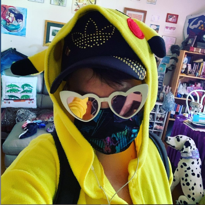 A person in a pikachu onesie and heart glasses and a vaporwave mask taking a selfie in a colorful room